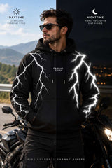 A man wearing a black hoodie with white lightning-bolt graphics stands outdoors beside a motorcycle, with the image split into daytime and nighttime views to show visibility. The hoodie has 'CARNAC BIKERS' printed on the chest.